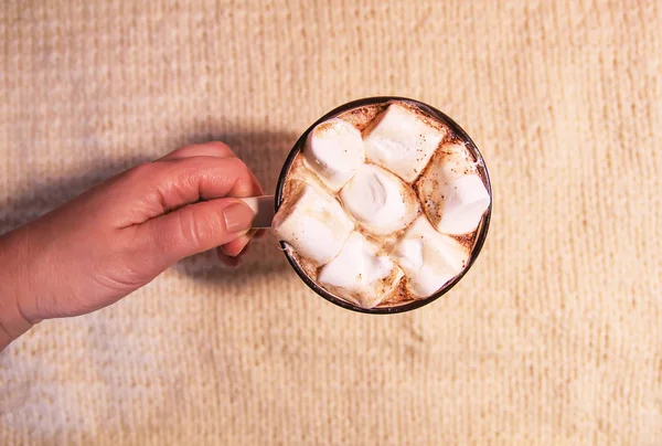 Woman's hand holding ceramic mug with hot fresh cocoa drink with marshmallows