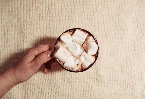 Woman's hand holding ceramic mug with hot fresh cocoa drink with marshmallows