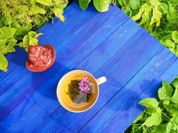 Mor taze çiçekli doğal bitki çayı ve tıbbi yakut yaprakları açık havada mavi tahta üzerinde seramik bardak..
