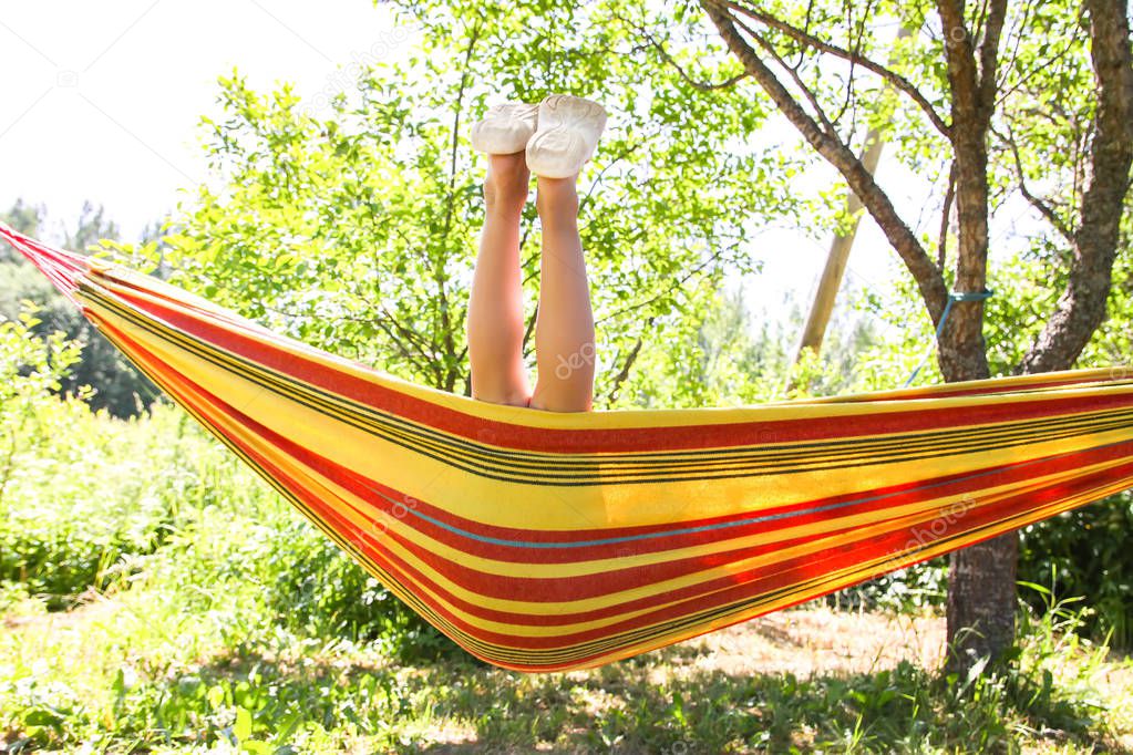 Adorable little girl with curly hair in colorful striped hammock on summer nature background in countryside.