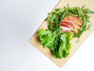 Kesme tahtasında taze yeşil marul ve roka yapraklarıyla dilimlenmiş jambon..