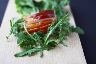 Kesme tahtasında taze yeşil marul ve roka yapraklarıyla dilimlenmiş jambon..