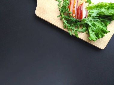 Kesme tahtasında taze yeşil marul ve roka yapraklarıyla dilimlenmiş jambon..