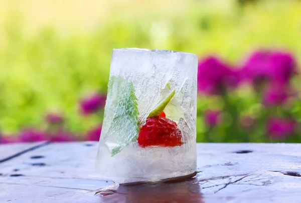 Cubo de gelo com folhas de morango, limão e hortelã verde fresco na superfície de madeira ao ar livre — Fotografia de Stock