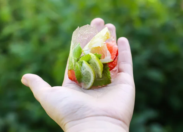 Cubo de hielo derretido con hojas de fresa, limón y menta verde fresca — Foto de Stock