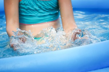 Küçük kız oynarken ve yaz aylarında açık yüzme havuzunda su püskürtme.