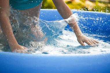 Küçük kız oynarken ve yaz aylarında açık yüzme havuzunda su püskürtme.