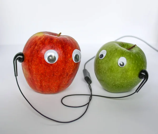 Красные и зеленые маленькие яблоки с милыми глазами и наушниками на белом фоне. Концептуальное фото . — стоковое фото