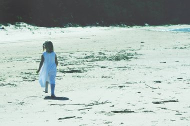 Küçük kız plajda beyaz bir elbiseyle oynuyor.