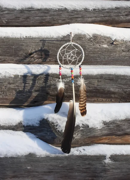 梦想捕手在古老的木制积雪覆盖墙壁的背景 用珠子和羽毛装饰的自制装饰品 — 图库照片
