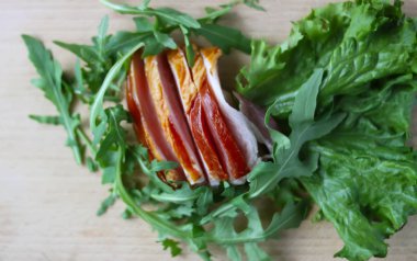 Kesme tahtasında taze yeşil marul yapraklarıyla dilimlenmiş jambon..