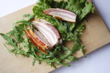 Kesme tahtasında taze yeşil marul ve roka yapraklarıyla dilimlenmiş jambon..