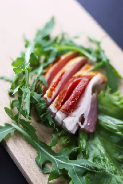 Jamón en rodajas con hojas de lechuga verde fresca en una tabla de cortar . —  Fotos de Stock