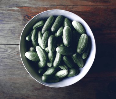 Tahta arka planda büyük bir fincanda taze salatalıklar.