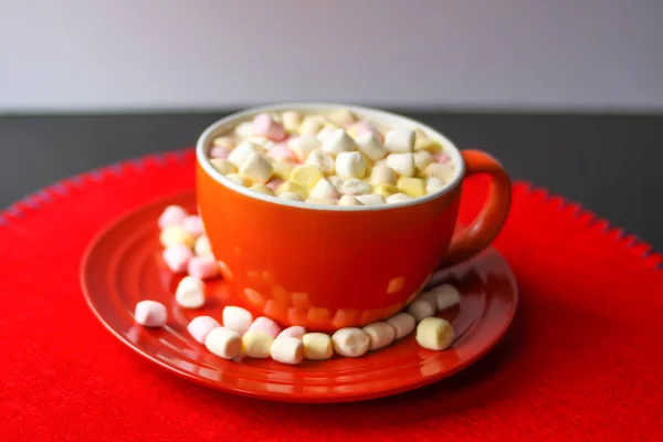 Cocoa drink with colorful small marshmallows on red background