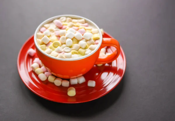 Cocoa drink with colorful small marshmallows on red background