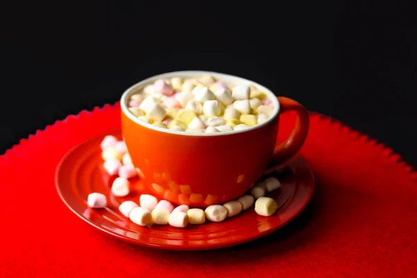 Cocoa drink with colorful small marshmallows on red background