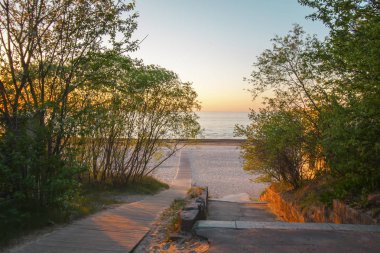 Bahar günbatımında Baltık Denizi sıcak gün ışığı. Yeşil ağaçlı ve tahta merdivenli bir manzara. Jurmala, Letonya, Doğu Avrupa 'daki kumsal.