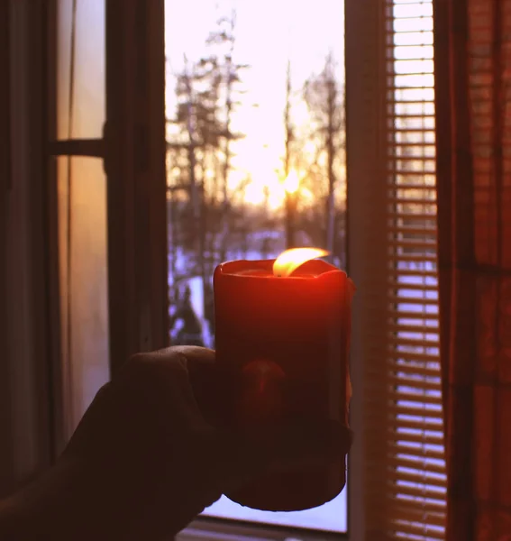 Red burning candle in a hand on window background. — Stock Photo, Image