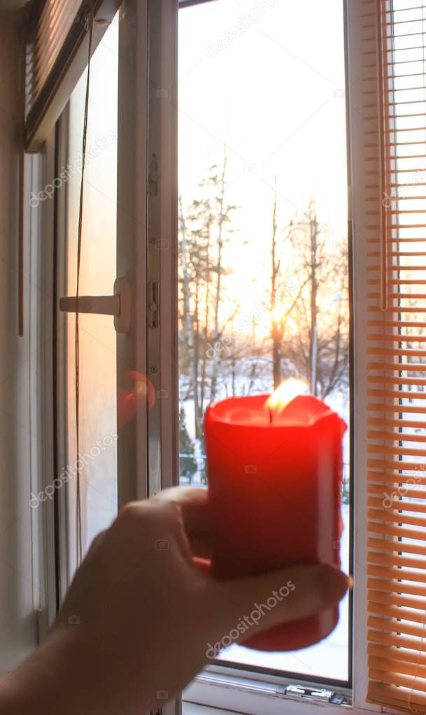 Red burning candle in a hand on window background.
