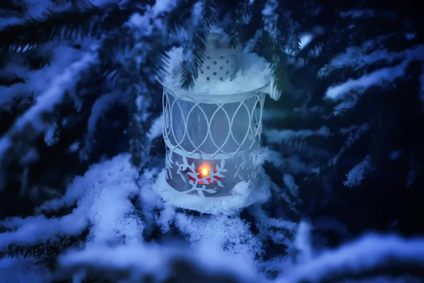 Decorative Christmas lantern with burning candle hanging on snow-covered fir- tree branch in a winter park. New year festive card, poster, postcard design. — Stock Photo, Image