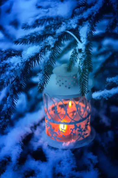 Decorative Christmas lantern with burning candle hanging on snow-covered fir- tree branch in a winter park. New year festive card, poster, postcard design. — Stock Photo, Image