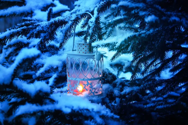 Dekorative Weihnachtslaterne mit brennender Kerze, die an einem schneebedeckten Tannenzweig in einem Winterpark hängt. Neujahrskarte, Plakat, Postkartendesign. — Stockfoto