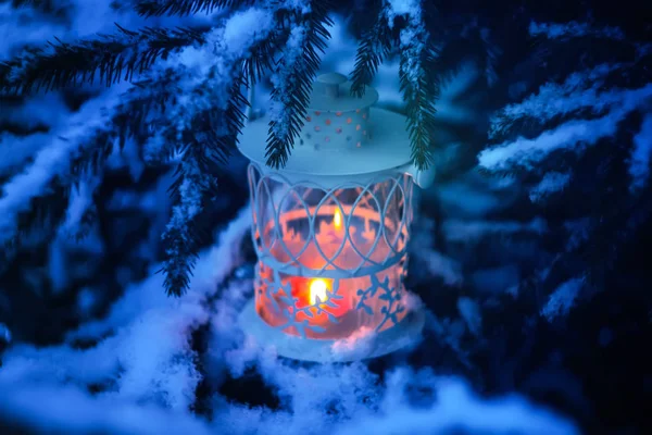 Декоративный рождественский фонарь с горящей свечой, висящей на заснеженной ветке елки в зимнем парке. Новогодняя праздничная открытка, плакат, дизайн открытки . — стоковое фото