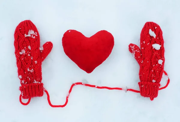 Rote Fäustlinge und dekoratives Herz aus Plüsch auf Schnee — Stockfoto