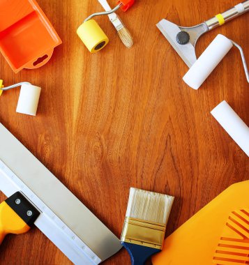 Sentetik fırçalar, köpük silindirler, spatula ve ahşap arka planda ev onarımı için diğer aletler.