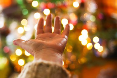 Kırsal kesimin iç kesimindeki süslenmiş Noel ağacının odağını çözmüş parlak bağları üzerinde bir kadın eli. Bulanık Yeni Yıl şenlik arka planı.