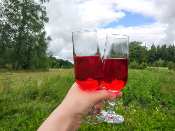 Two glasses with homemade red vine in a hand on farm yard background in a countryside at summer.