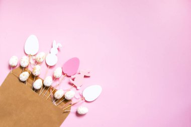 Geleneksel dekorlu Paskalya kompozisyonu. Dekoratif renkli yumurta ve kağıt zarf içinde açık pembe kağıt arka planda tavşan ahşap figürler..