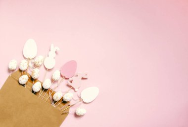 Geleneksel dekorlu Paskalya kompozisyonu. Dekoratif renkli yumurta ve kağıt zarf içinde açık pembe kağıt arka planda tavşan ahşap figürler..