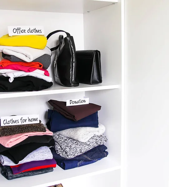 Kleding en accessoires sorteren in huis garderobe op witte plank achtergrond. Kantoorkleding, kleding voor thuis, briefjes van donateurs. — Stockfoto