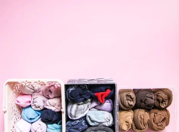 Vêtements colorés rangement vertical dans la garde-robe à domicile. Vêtements en plastique et boîte textile sur fond rose doux . — Photo
