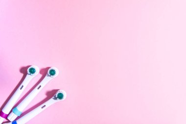 Yumuşak açık pembe arka planda iki elektrikli diş fırçası.