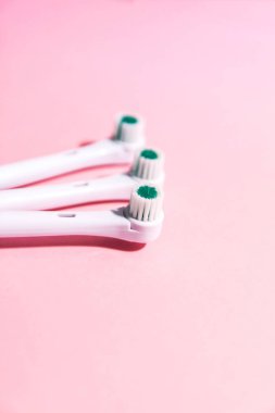 Yumuşak açık pembe arka planda iki elektrikli diş fırçası.