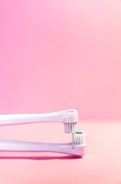 Yumuşak açık pembe arka planda iki elektrikli diş fırçası.