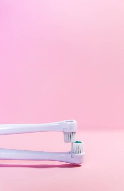 Yumuşak açık pembe arka planda iki elektrikli diş fırçası.