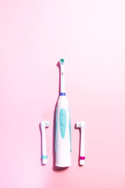Yumuşak açık pembe arka planda iki elektrikli diş fırçası.