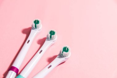 Yumuşak açık pembe arka planda iki elektrikli diş fırçası.