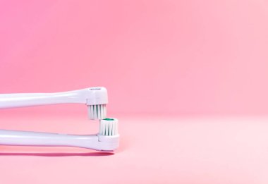 Yumuşak açık pembe arka planda iki elektrikli diş fırçası.