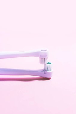 Yumuşak açık pembe arka planda iki elektrikli diş fırçası.