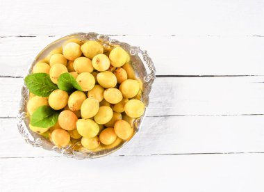 Taze sarı erik. Beyaz tahtalar arka planda bir tabak olgun meyve.