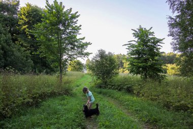 Küçük kız köpeğiyle ormanda yürüyor.