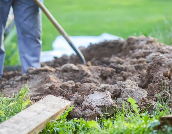 Genç adam bir kürekle toprağı kazıyor.