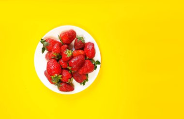 Beyaz bir tabakta, parlak sarı arka planda kırmızı çilekler. Taze fuit bayrağı.