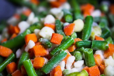 Donmuş durumda fasulye ve havuçlu karnabahar çiçekleri. Metal tavada buzun içindeki çiğ sebzeler..