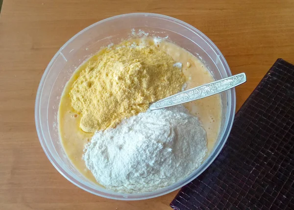 Preparation for the dough to the cake with gluten-free rice and corn flour in a transparent plastic bowl and a brown notepad next to